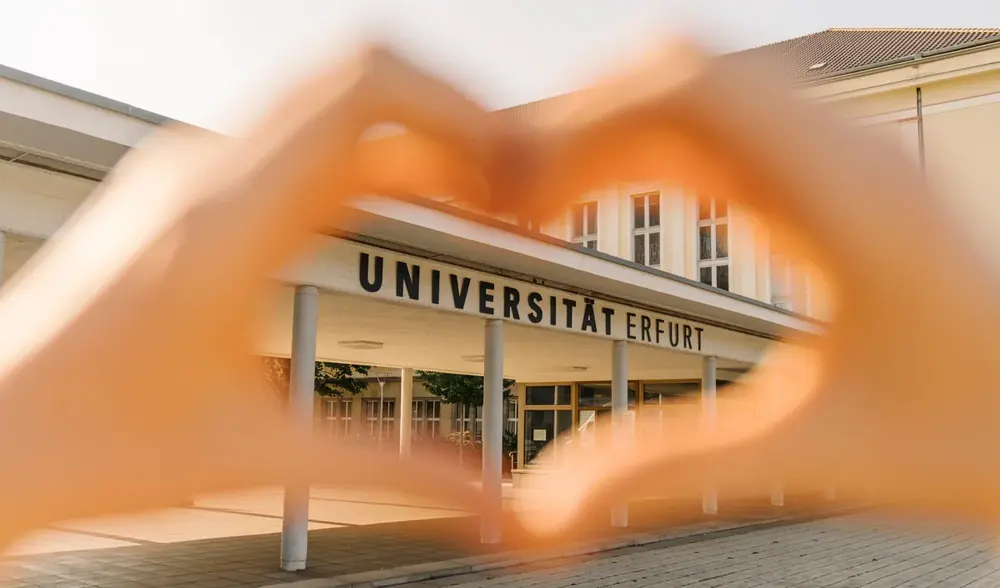 Hände in Herzform vor dem Haupteingang der Uni Erfurt
