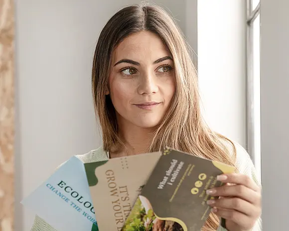Eine junge Frau hält drei Flyer in der Hand