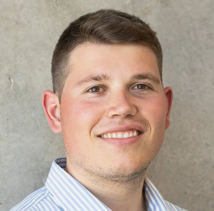 Porträtfoto von Elias, Student der Wirtschaftswissenschaft, freundlich lächelnd, kurze dunkelblonde Haare, hellblaues Hemd vor grauem Hintergrund