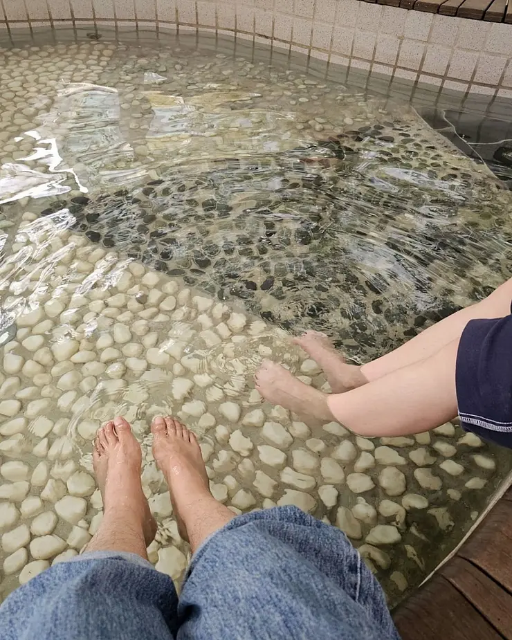 Zwei unbedeckte Füße baumeln im Wasserbecken, das mit hellen Fliesen abschließt
