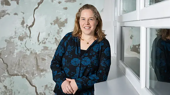 A woman in a patterned top leans against a window