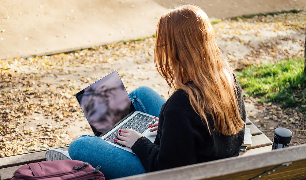 Eine Studentin sitzt mit ihrem Laptop auf einer Parkbank