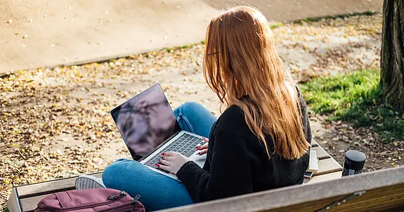 Eine junge Frau sitzt mit einem Computer auf einer Bank