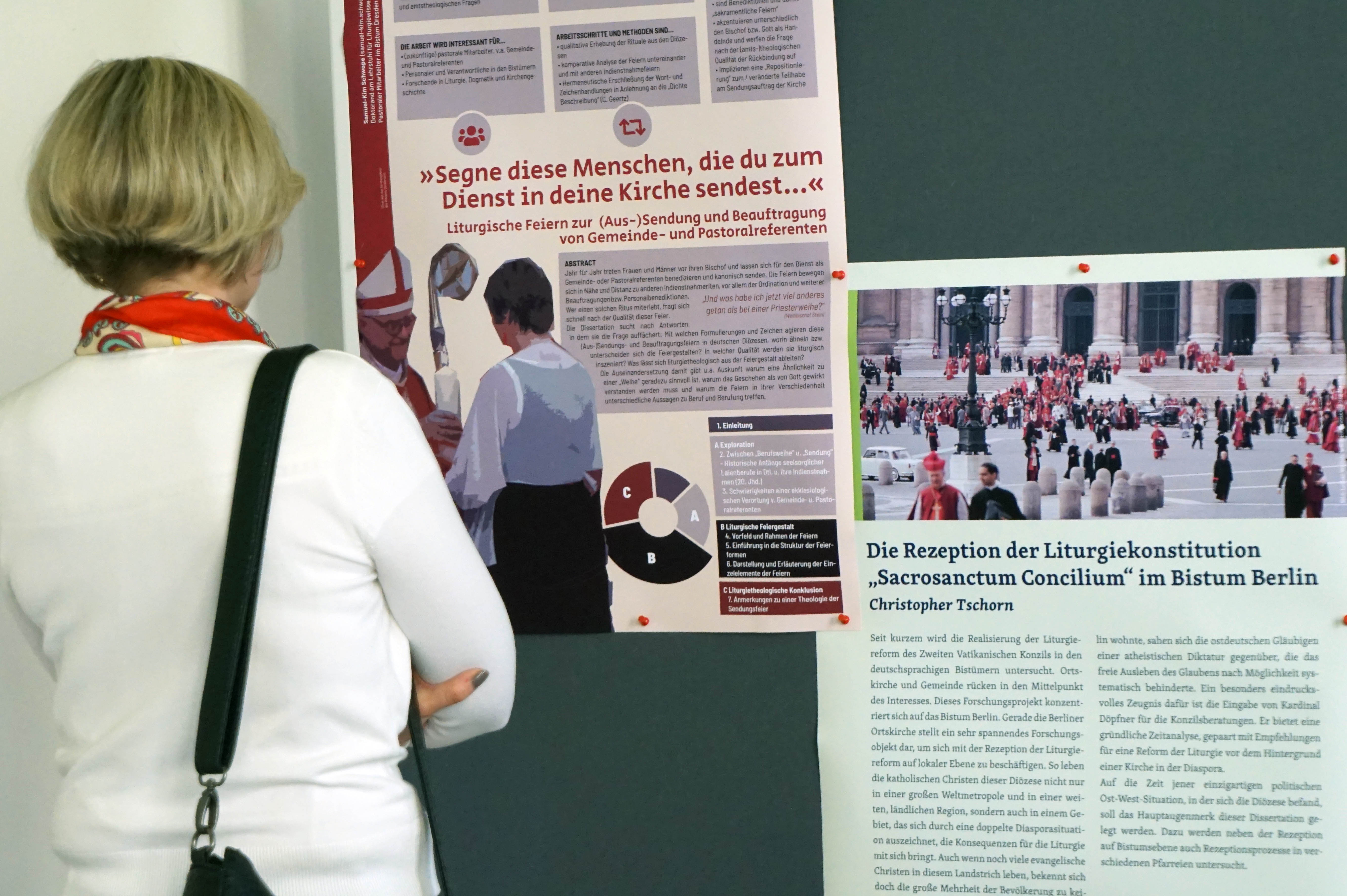 Eine Frau steht vor zwei Postern (Posterpräsentation im Rahmen des Alumnitreffens)